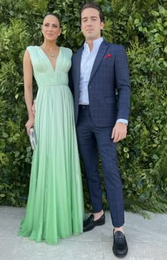 a man and woman standing next to each other in front of a green plant wall