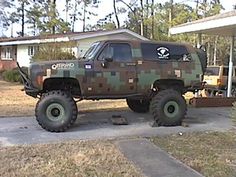 a camo truck parked in front of a house with two large tires on it