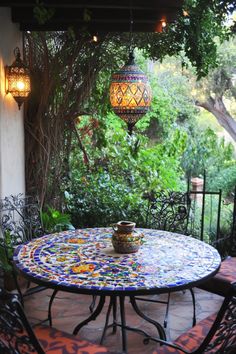 a mosaic table and chairs on an outdoor patio with lights hanging from the ceiling above it