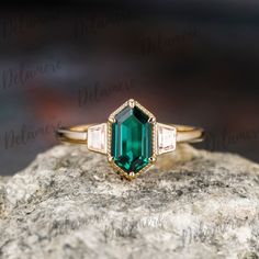 an emerald and diamond ring sitting on top of a rock