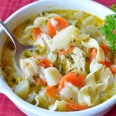 a bowl of chicken noodle soup with carrots and parsley on the side