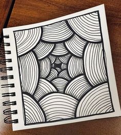 a spiral notebook with black and white drawing on it, sitting on top of a wooden table