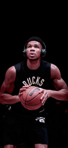 a man holding a basketball in his right hand and wearing headphones on top of it