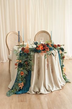 a table with flowers and candles on it in front of a curtained wall, next to two chairs