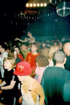 a crowd of people standing around each other at a concert or club with lights on