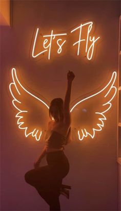 a woman standing in front of a neon sign that says let's fly