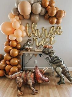 two dinosaurs are standing next to each other in front of balloons that spell out three sides