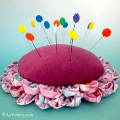 a pink pillow with colorful pins sticking out of it's center and sitting on top of a pile of fabric