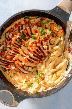 a skillet filled with chicken and vegetables on top of a blue table cloth next to a wooden spatula