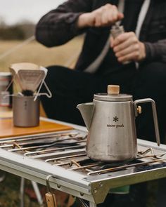 a person sitting at a table with a coffee pot on top of it, next to a stove