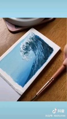 someone is drawing a wave on paper with a brush