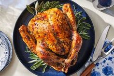 a roasted turkey on a plate with rosemary garnishes and silverware next to it