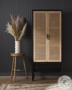 a tall wooden cabinet sitting next to a plant on top of a table in front of a black wall