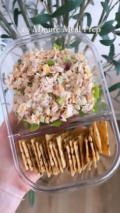 a hand holding a plastic container filled with salad and crackers