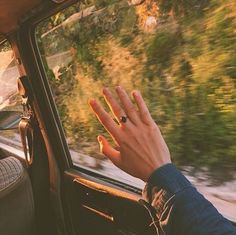 a person's hand out the window of a car with trees in the background