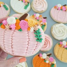 a person holding up a decorated cookie in front of some cookies on a table with frosting