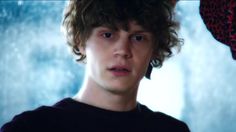 a young man with curly hair wearing a black t - shirt looking at the camera