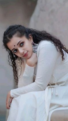 a woman sitting on top of a white couch next to a wall with her hands on her knees