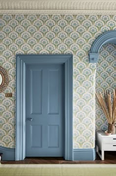 a blue door in front of a wallpapered room with a mirror and vase