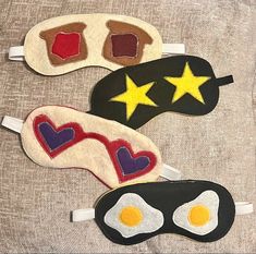 three sleep masks with hearts, stars and eggs on them sitting on a bed sheet