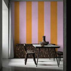 a dining table with two chairs and a vase on it in front of a striped wall