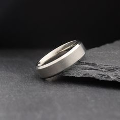 two wedding bands sitting on top of each other in front of a black stone slab