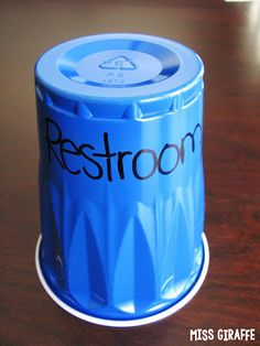 a blue trash can sitting on top of a wooden table with the word restroom written on it