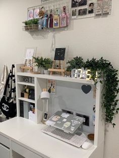 a white desk topped with a laptop computer next to a shelf filled with pictures and plants