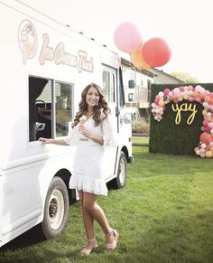 a woman standing in front of a food truck with balloons on the side of it