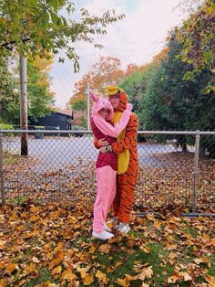 two people dressed as winnie the pooh and tigger hugging in front of a fence