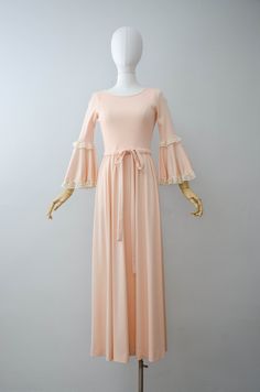 A peach maxi dress with a stretchy ribbed bodice. The half sleeves and skirt are done in a silky polyester with the bell sleeves being trimmed in lace. A drawstring tie is found at the waist and it has a back zip closure. ☛ m e a s u r e m e n t s ☚ Bust: 32-36 Waist: 27-34 Hips: open Shoulders: 11.5-14 Length: 55 ☛ d e t a i l s ☚ Era: 1970s Material: polyester Condition: excellent ☛ v i s i t t h e s h o p ☚ https://etsy.me/2Nd23kg ☛ instagram ┇ poppycockvintage ☛ facebook ┇ poppycockvintage Elegant Summer Maxi Dress With Bell Sleeves, Spring Bell Sleeve Stretch Dresses, Elegant Bell Sleeve Maxi Dress For Summer, Spring Stretch Bell Sleeve Dresses, Spring Beige Stretch Maxi Dress, Beige Stretch Maxi Dress For Spring, Feminine Fitted Peach Maxi Dress, Peach Fitted Floor-length Maxi Dress, Fitted Apricot Maxi Dress For Spring