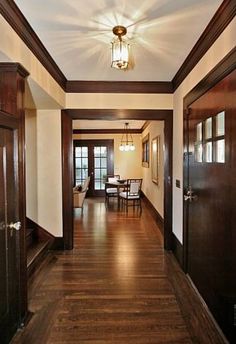 a long hallway with wood floors and wooden door frames on both sides, leading to the dining room