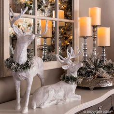 two white deer figurines sitting on top of a table next to candles and a mirror