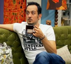 a man sitting on a couch holding a coffee cup and looking up at the camera