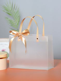 a white bag with a gold bow on it sitting on a table next to a candle