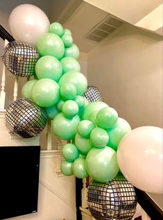 a bunch of green and white balloons hanging from the side of a stair case in a house