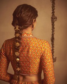 a woman with braids in her hair and wearing an orange blouse, standing next to a metal pole