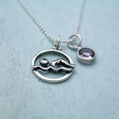 a silver necklace with an image of a bird on it's back and a small purple stone in the middle