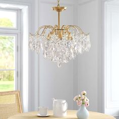 a chandelier hanging from the ceiling over a table with flowers and cups on it