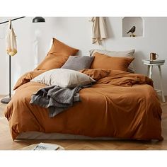 a bed with orange sheets and pillows in a white room next to a wooden floor