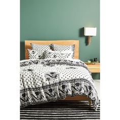 a bed with black and white patterned comforter next to a wooden headboard in a green room