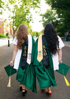 two women in graduation gowns walking down the street with tassels on their backs