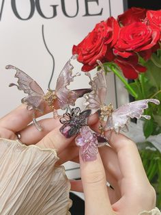 the woman is holding two small butterflies in her hand next to flowers and a vase with red roses