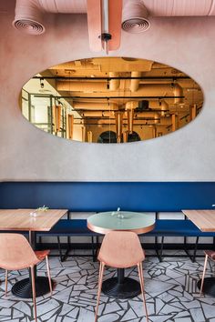 the interior of a restaurant with blue booths and wooden tables in front of an oval mirror