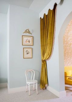 a white chair sitting in front of a window next to a wall with pictures on it