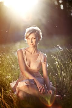 a woman sitting in tall grass with the sun shining behind her