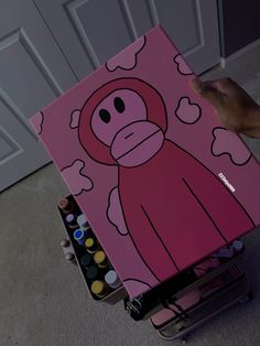 a person is holding up a pink monkey painting