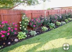 a garden filled with lots of flowers next to a wooden fence and green grass covered yard