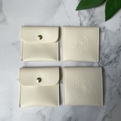 three monogrammed white leather business cards cases on a marble surface with green leaves