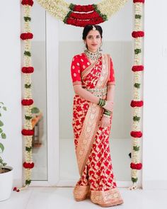 a woman in a red and gold bridal outfit standing under a floral arch with flowers on it